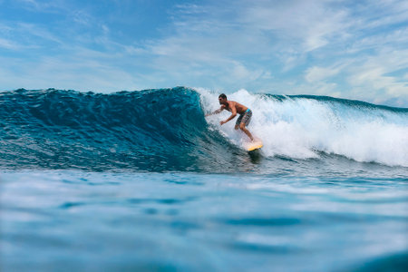 Male surfer on a blue wave at Bali islandの写真素材
