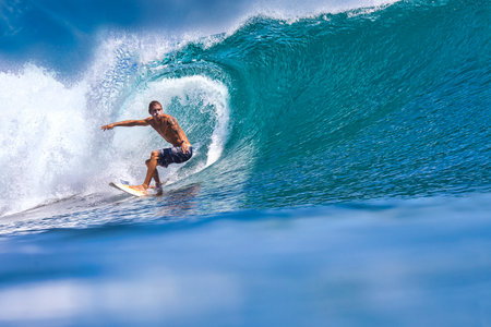 Male surfer on a blue wave at sunny day
