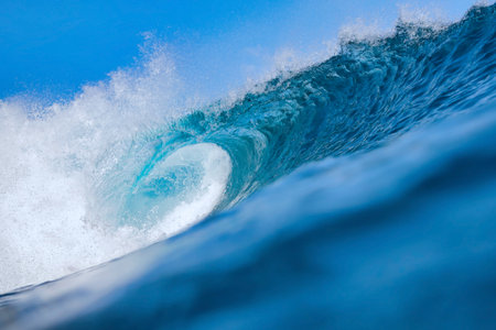 Massive blue ocean wave curling, bright turquoise barrel breaking with foamy crest and spray, sunlightの写真素材