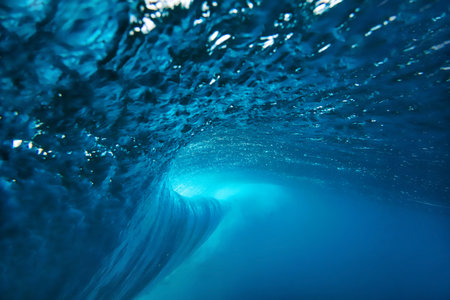 Underwater view breaking ocean wave tunnel deep blue barrel curling above, light filtering through...