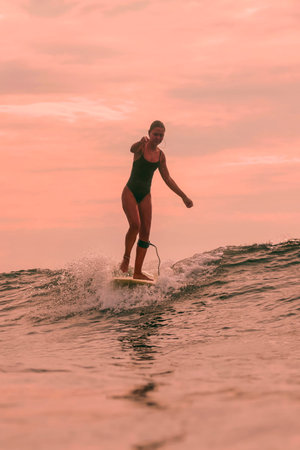 Woman Balancing On Surfboard At Sunset, Relaxed Cruise With Raised Arm And Steady Posture, Warm Sky, Smoothの写真素材