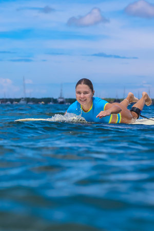 Young Woman Paddling On Surfboard Smiling, Shallow Ocean Lens View With Gentle Waves, Bright Blue...