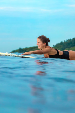 Young Woman Training On Surfboard At Dusk With Steady Focus, Endurance Session And Calm Coastal Atmosphereの写真素材