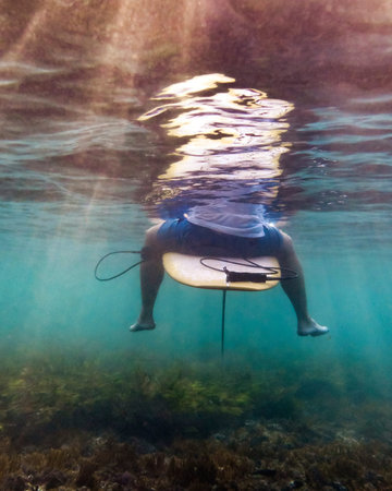 Surfer Seated On Surfboard Beneath Surface, Competitive Athlete Scouting Incoming Swell, Feet Brushing Seabedの写真素材