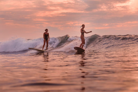 Two Surfers Riding Synchronized Waves, Matching Posture And Coordinated Turns, Twilight Sky, Twin Silhouettes,の写真素材