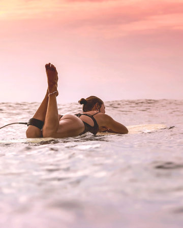Young Woman Resting On Surfboard In Calm Sea, Legs Raised And Relaxed, Scanning Soft Clouded Horizon, Patientの写真素材