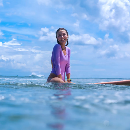 Young Woman Surfer Sitting On Board Smiling Waiting Amid Calm Ocean And Blue Sky. Purple Rashguard, Gentleの写真素材