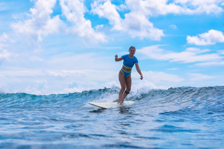 Female Surfer Riding High Crest With Arms Raised, Peak Moment Of Triumph, Dramatic Backlit Cloudscape,の写真素材