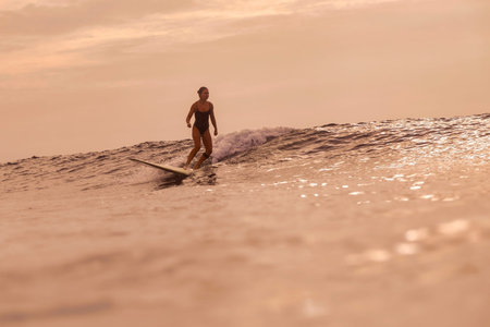 Woman Finishing Surf Session At Sunset, Relaxed Stride On Board With Soft Sky And Gentle Swell,...