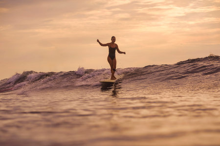 Woman Cruising Wave Under Pink Sky At Sunset, Relaxed Silhouette On Longboard With Soft Backlight And Gentleの写真素材
