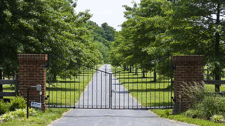 Iron gates open and close to estate on a treelined road.