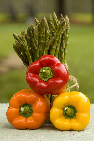 Three assorted peppers stacked in front of tall asparagus.の写真素材