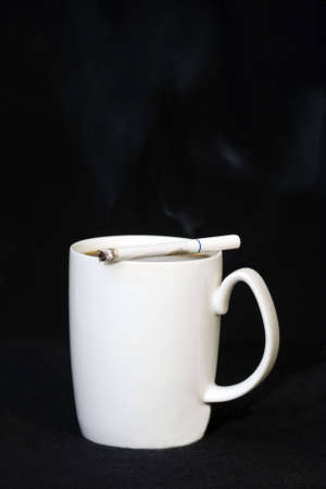 Coffee cup with cigarette laying across top with smoke in airの写真素材