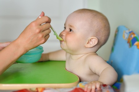 mother feeding baby boy at home kitchen.の写真素材