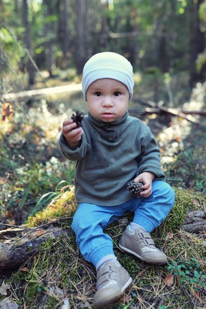 Funny little boy playing with pine cones sitting on the floor.の写真素材