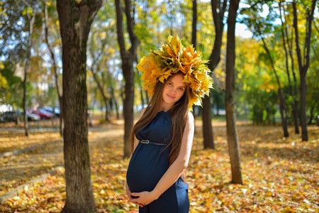 Young pregnant woman in the autumn park with wreath of maple leaves.の写真素材