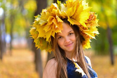 Young woman in the autumn park with wreath of maple leaves.の写真素材