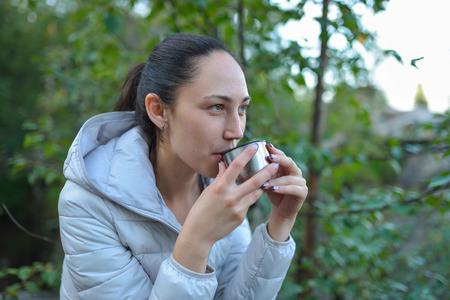 Young beautiful woman drinking hot tea from a thermos cup outdoors.の写真素材