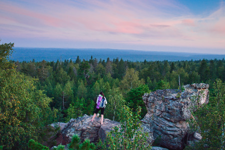 Lady hiker with backpack standing on top of the mountain and enjoying valley view at sunsetの写真素材