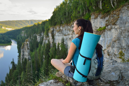 Young woman with backpack sitting on cliff's edge at high mountain.の写真素材