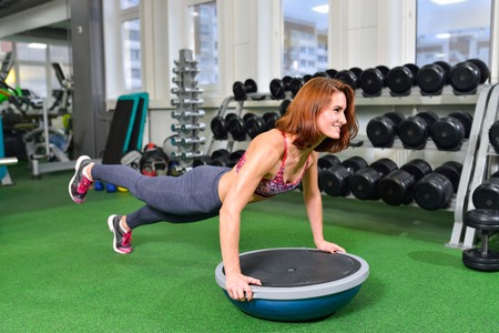 Fitness woman planking doing the body weight exercise for core strength training in gym with bosu balance trainer.の写真素材