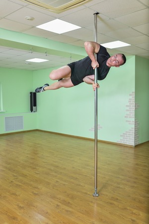 Young strong male dancer performing dancing moves on the pole.の写真素材