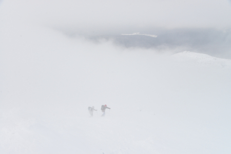 Group of people hiking in winter mountains during a snow storm, walking over clouds.の写真素材
