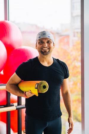 Happy Indian man at the gym holding yoga mat after his practiceの写真素材