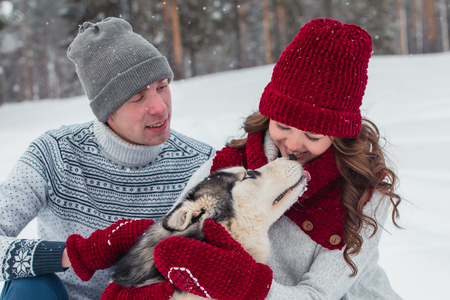 Young couple with a Husky dog walking in winter park, Man and woman hugging a dog.の写真素材