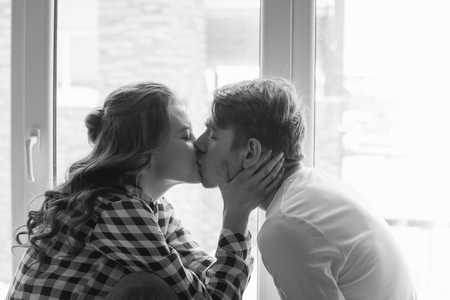 Portrait of beautiful romantic young couple, man woman in love hugging, kissing, indoors at home, black and whiteの写真素材