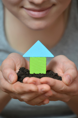 Female hands holding a piece of land with wooden houseの写真素材