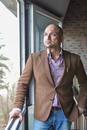 Cheerful and stylish indian man standing near the windowの写真素材