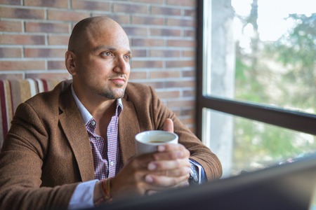 Indian stylish man drinking coffee, dreamy looking up and thinking