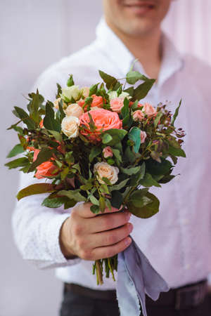 close up of young man in white shirt giving bouquet of flowers as surprise, focus on roses.の写真素材