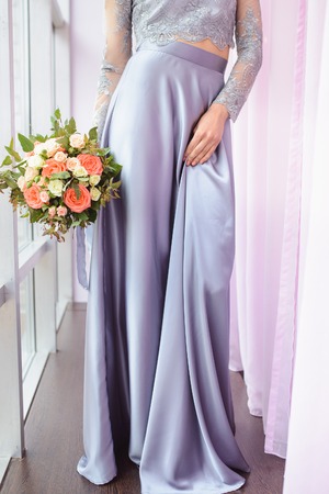 Beautiful woman in a plum dress holding a bouquet of roses, closeup detail shoot, focus on flowersの写真素材