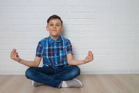 Cute boy is meditating and smiling while sitting in lotus position on the floor, copu space is availabe.の写真素材