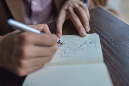 Businessman hands with pen writing notebook on wooden desk table close up. Business planning concept.の写真素材
