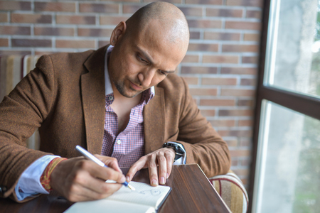 Serious indian man making some notes in his notebook, business plan or diary writing.の写真素材