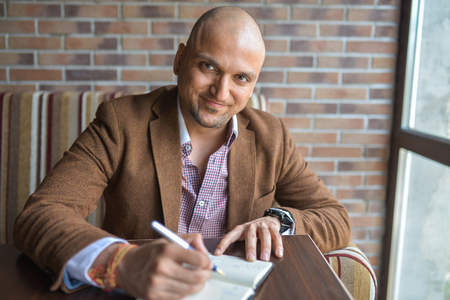 Happy handsome indian businessman making some notes in his notebook, business plan or diary writingの写真素材