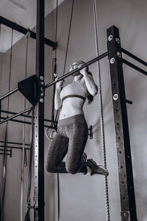 Sexy young fit woman doing pull-up on on a crossbeam - horizontal bar. Strong Female fitness at gym.