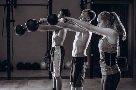 Healthy fit young athletes doing exercises with kettlebells at gym, men and women during weight lifting workoutの写真素材