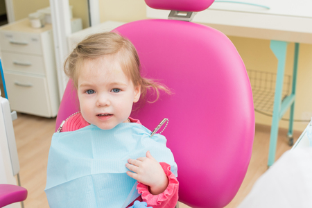 Cute Little girl sitts in dental chair at dentist office, closeup portraitの写真素材