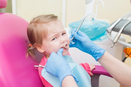 Cute Little girl sitts in dental chair at dentist office, closeup portraitの写真素材