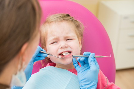 Cute Little girl sitts in dental chair at dentist office, closeup portraitの写真素材