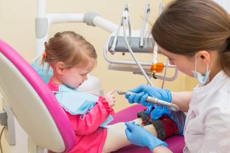 Little girl sitts in dental chair at dentist office talking with female doctorの写真素材