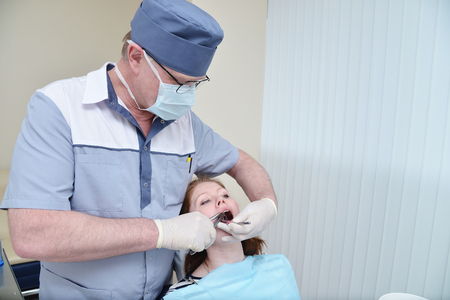 Male Dentist during extraction procedure with forceps removing patient tooth. Health care dentistry medicine concept.の写真素材