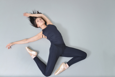 Young woman ballerina lying and stretching on the floor at ballet studio, view from above.の写真素材