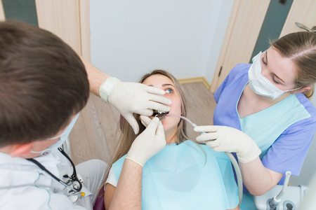 Male dentist treating patient teeth with assistantの写真素材