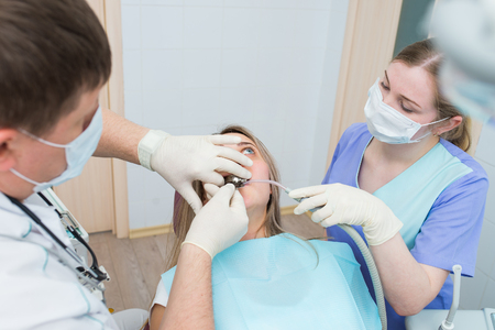 Male dentist treating patient teeth with assistantの写真素材