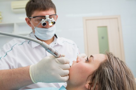 Doctor dentist treats teeth of a beautiful young girl patient. The woman on reception at the dentist. Doctor dentist treats tooth.の写真素材